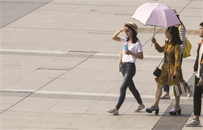 西湖文化广场，行人穿起短袖，撑起了遮阳伞。 